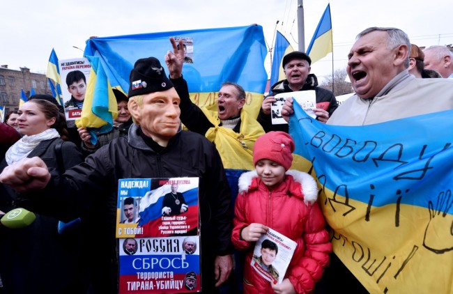 Protesters shout slogan "Free Savchenko!" and hold portraits of jailed female Ukrainian pilot Nadiya Savchenko during a rally in front of Russian embassy in Kiev on March 9, 2016. The placard held by the man wearing a mask of Russian President Vladimir Putin reads : "Throw off the terrorist, tyrant and murderer !" Ukraine on March 9, 2016 demanded that Moscow "immediately" free Nadiya Savchenko, a hunger-striking military helicopter pilot on trial in Russia. / AFP / SERGEI SUPINSKY