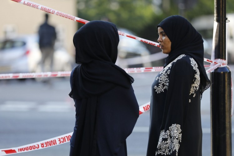 Two women watch proceedings at the security cordon at the scene in Finsbury Park area of north London after a vehichle hit pedestrians, on June 19, 2017.  One man was killed and eight people hospitalised when a van ran into pedestrians near a mosque in north London in an incident that is being investigated by counter-terrorism officers, police said on Monday. The 48-year-old male driver of the van "was found detained by members of the public at the scene and then arrested by police," a police statement said.  / AFP PHOTO / Tolga AKMEN