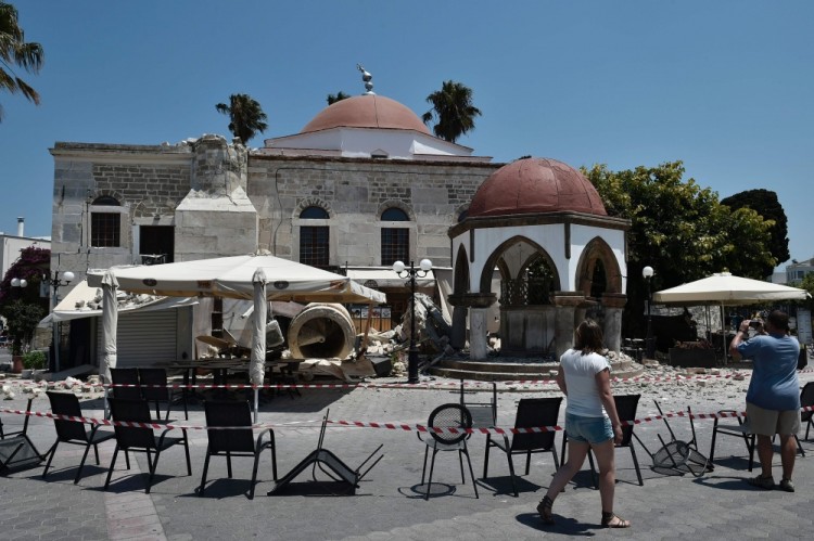 Tourists look at a destroyed mosque at a central square on the Greek island of Kos on July 21, 2017, following an earthquake which struck the region.  A strong 6.7-magnitude undersea quake hit the Greek holiday island of Kos and the Turkish resort of Bodrum on Friday, killing two people and injuring dozens in areas abuzz with nightlife. The epicentre of the quake was approximately 10.3 kilometres (6.4 miles) south of the southwestern resort Bodrum, a magnet for holidaymakers in the summer, and 16.2 kilometres east of the island of Kos in Greece, the US Geological Survey said. / AFP PHOTO / LOUISA GOULIAMAKI