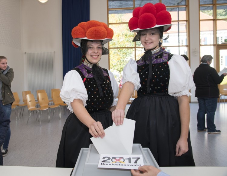 Christina Lehmann (L) and Jana Bruestle wear traditional dresses of the Black Forest area including the typical "Bollenhut" pompon hats as they cast their ballots at a polling station in Gutach near Freiburg, southwestern Germany, during general elections on September 24, 2017. Polls opened in Germany in a general election expected to hand Chancellor Angela Merkel a fourth term, while the hard-right Alternative for Germany (AfD) party is predicted to win its first seats in the national parliament. / AFP PHOTO / THOMAS KIENZLE