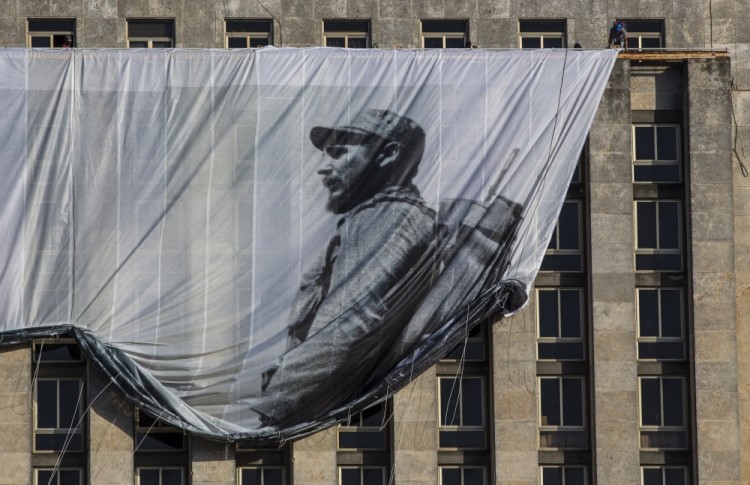 Men hang a giant banner with a picture of Cuba's late leader Fidel Castro as a young revolutionary, from the Cuban National Library building in Havana, Cuba, Sunday, Nov. 27, 2016. Cuba's government declared nine days of national mourning after Castro died Friday and this normally vibrant city has been notably subdued. (AP Photo/Desmond Boylan)