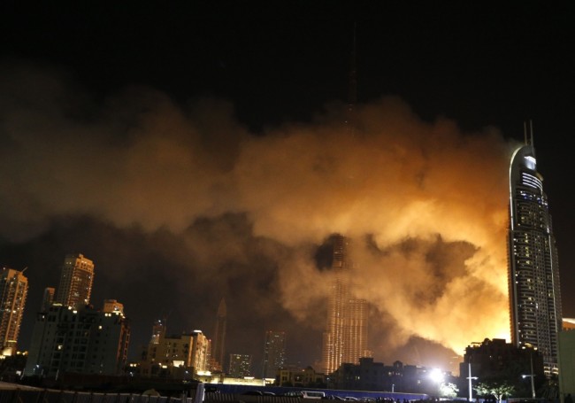 Smoke billows from the Address Downtown Hotel, after it caught on fire hours earlier, past fireworks, near the Burj Khalifa, the world's tallest tower in Dubai, on January 1, 2015. At least 16 people were injured when a huge fire ripped through a luxury 63-storey hotel, the Address Downtown, where crowds were gathering to watch New Year's Eve celebrations. The cause of the blaze was not immediately known but the building was safely evacuated. AFP PHOTO / KARIM SAHIB