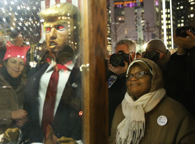 People pause to listen to a glass-encased, talking replica of Donald Trump as the puppet implores listeners to "See How Great America's Future Is," in front of the Trump International Hotel, Thursday, Jan. 19, 2017, in New York. President-elect Donald Trump, a New Yorker, is scheduled to take the oath of office Friday in Washington. (AP Photo/Kathy Willens)
