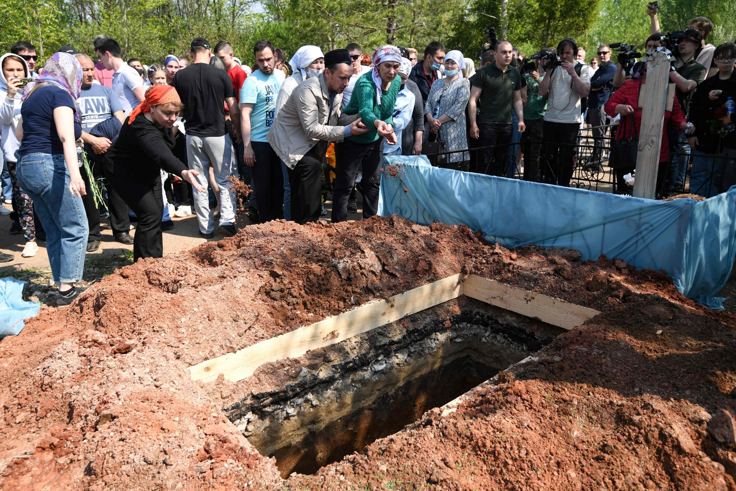 Люди бросают землю в могилу, куда опустили гроб с учительницей английского языка Эльвиры Игнатьевой. Фото NATALIA KOLESNIKOVA / TASS / Scanpix / Leta