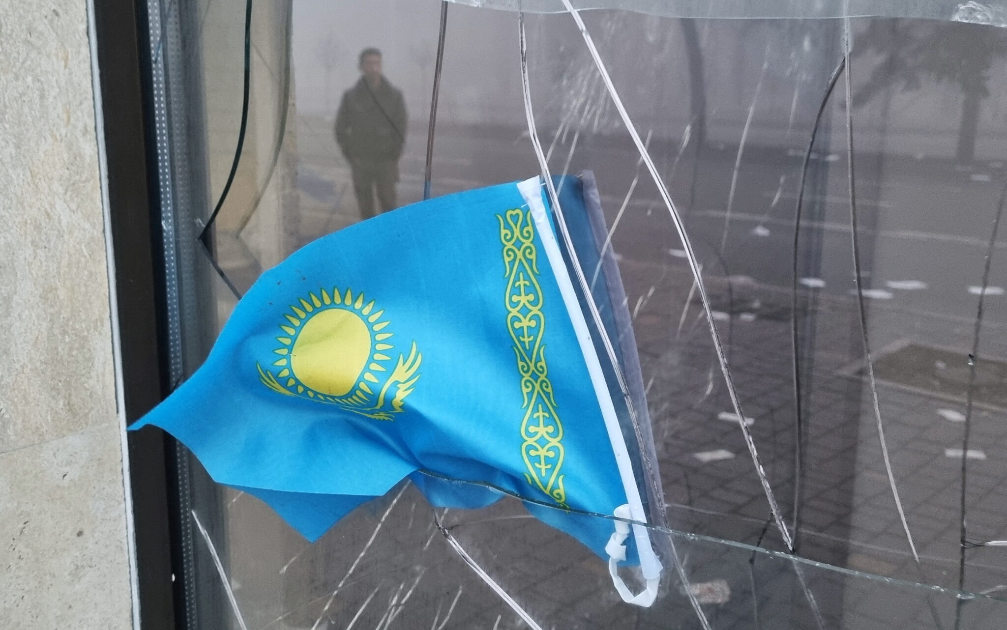 Государственный флаг Казахстана на фоне разбитой витрины в Алматы. Фото REUTERS/Pavel Mikheyev/Scanpix/Leta