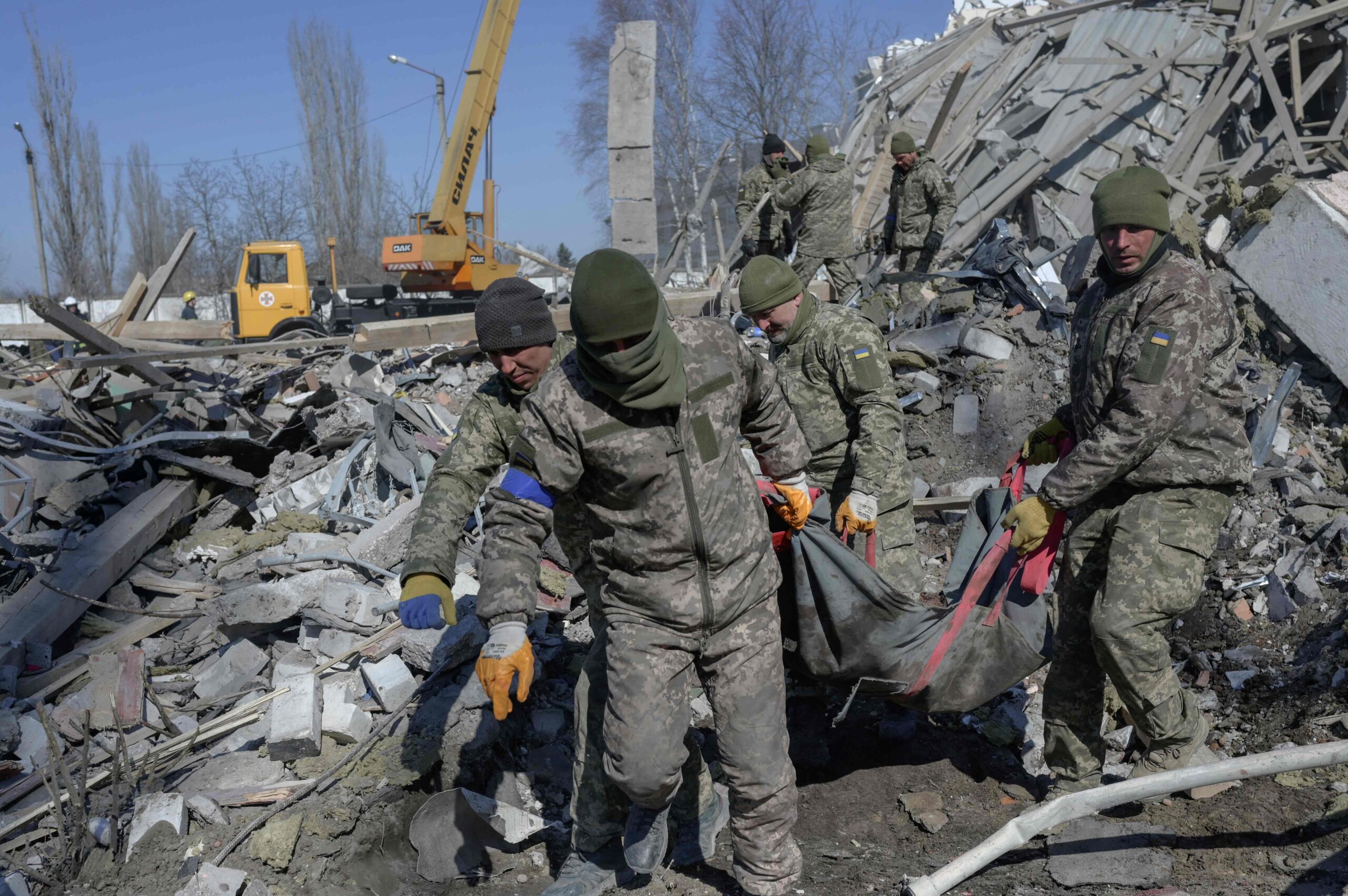 Украинские солдаты несут мертвого сослуживца через развалины военного училища, обстрелянного накануне российскими ракетами. Николаев. 19 марта 2022 года. Фото BULENT KILIC/AFP/Scanpix/Leta