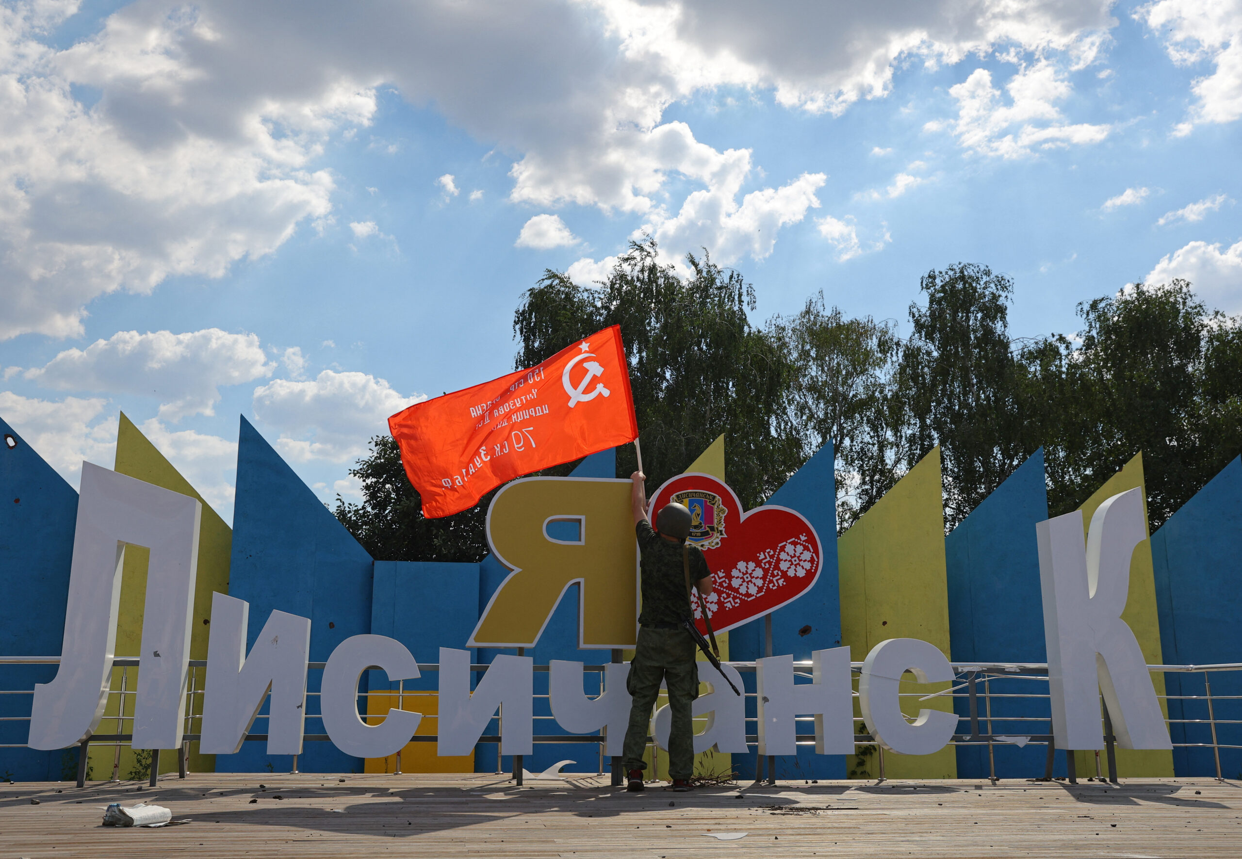 Военнослужащий пророссийских сил вывешивает флаг над монументом “Я люблю Лисичанск”. 4 июля 2022 года. Фото REUTERS/Alexander Ermochenko/Scanpix/LETA