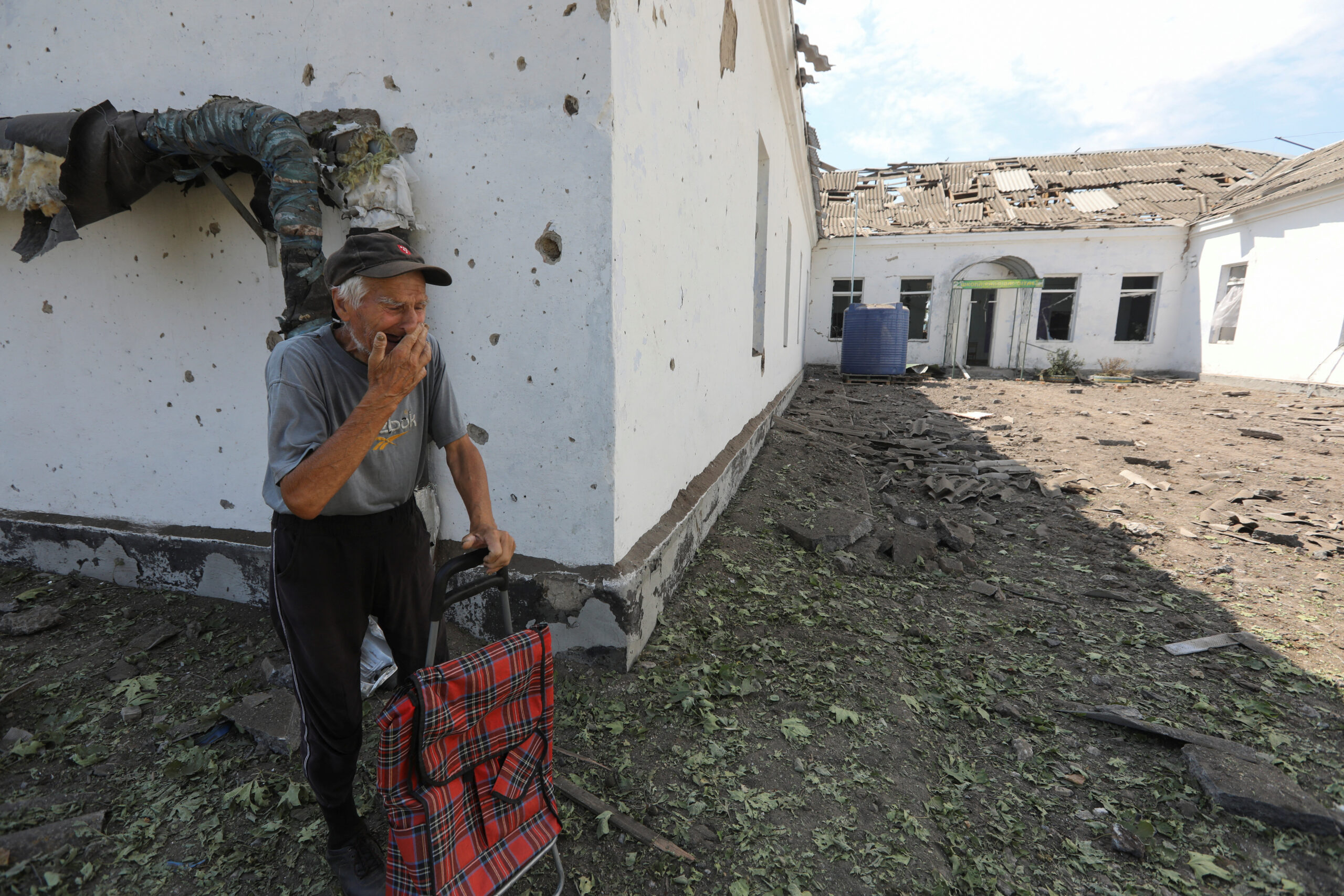 Местный житель рядом с поврежденным ракетным обстрелом зданием школы, Николаев. 28 июля 2022 года. Фото REUTERS/Mykola Tymchenko/Scanpix/LETA