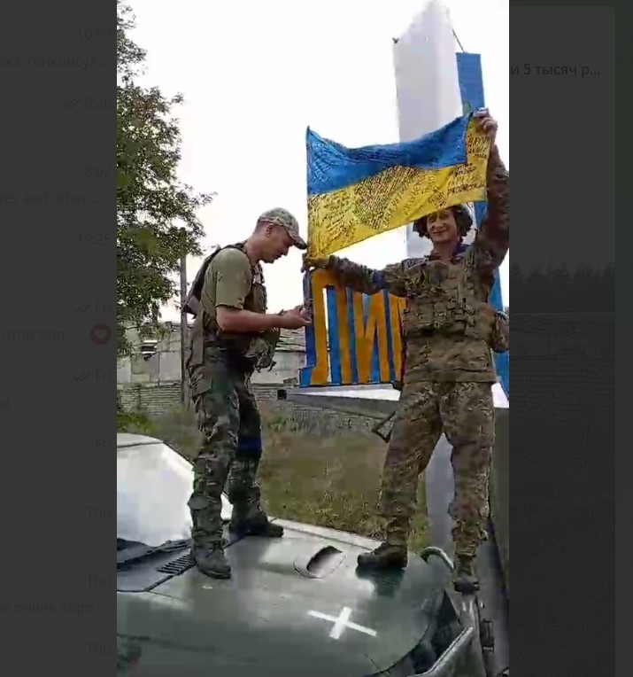 Скриншот из записи, на которой, предположительно украинские военные вешают флаг Украины на стелу при въезде в Лиман.