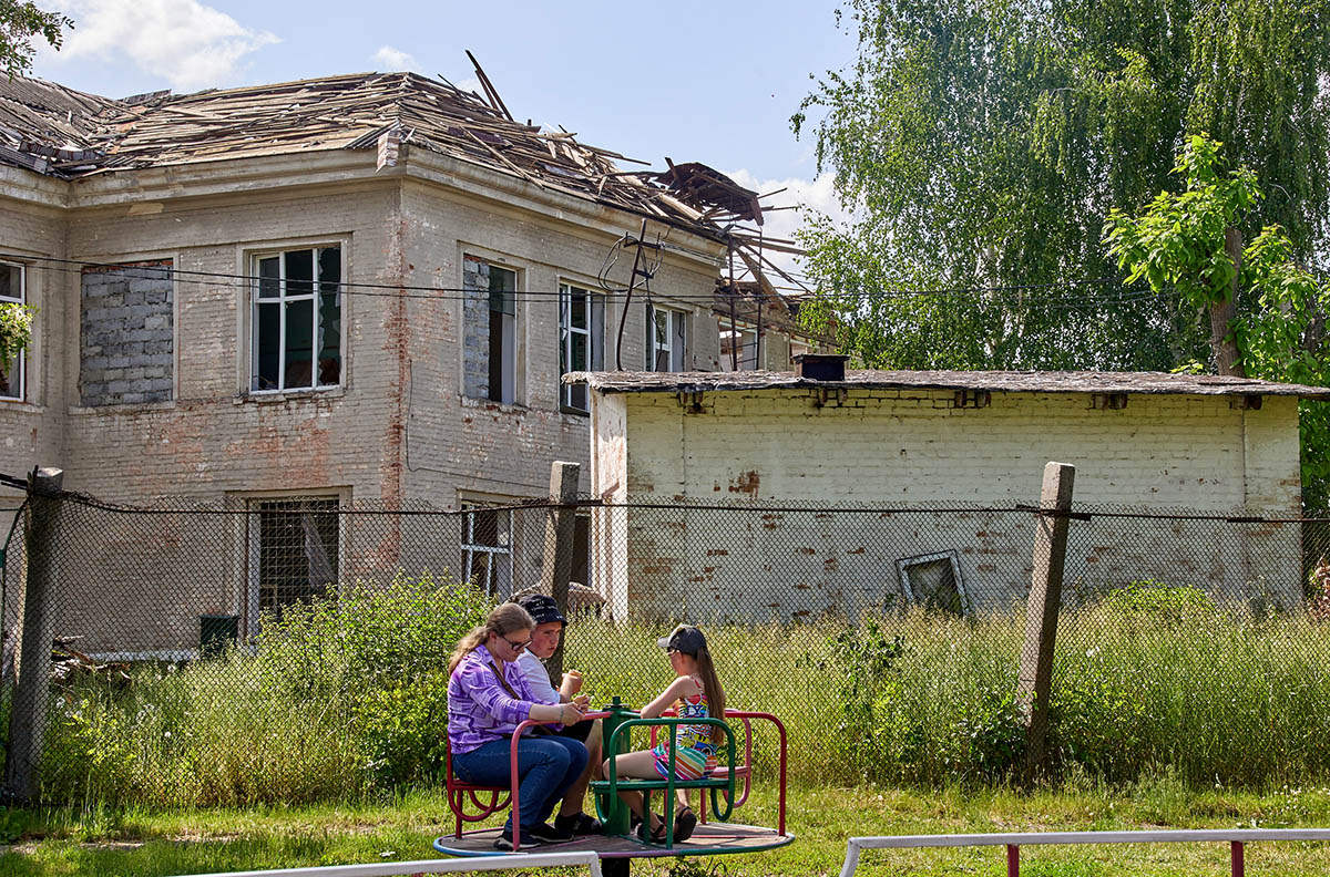 Дети сидят на карусели возле разрушенной школы в городе Мерефа, Харьковская область, Украина. Фото SERGEY KOZLOV/EPA/Scanpix/LETA