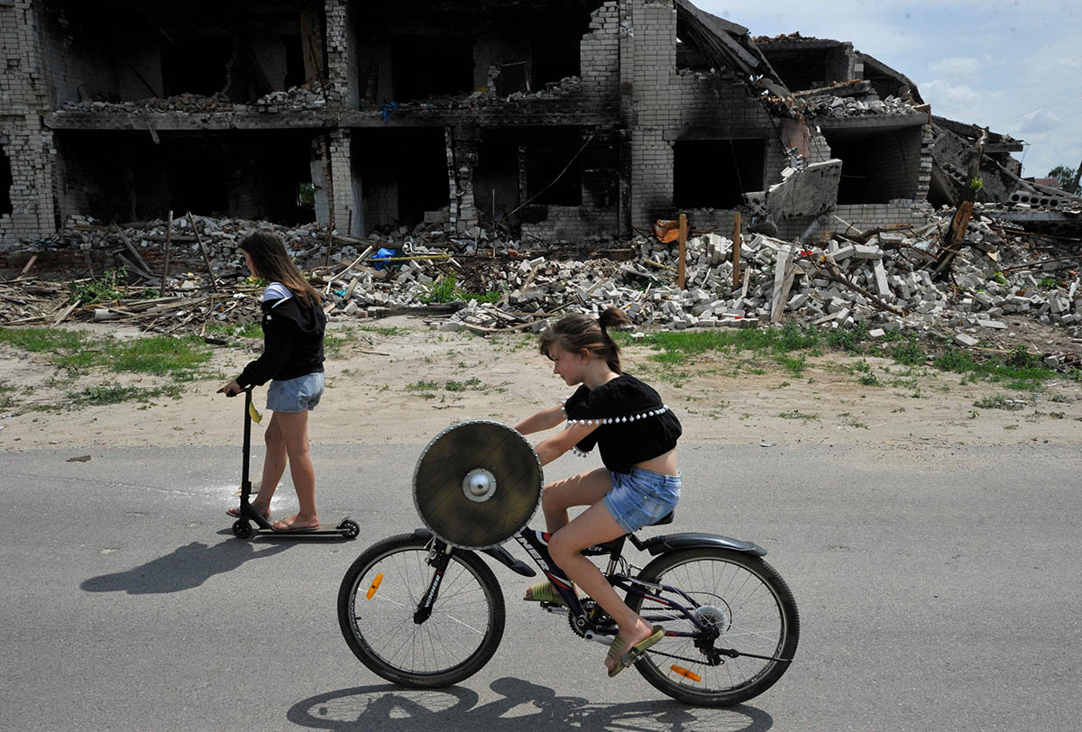 Девочки едут по дороге мимо разрушенного здания в селе Новоселовка под Черниговом, Украина. Фото Sergei CHUZAVKOV/AFP/Scanpix/LETA
