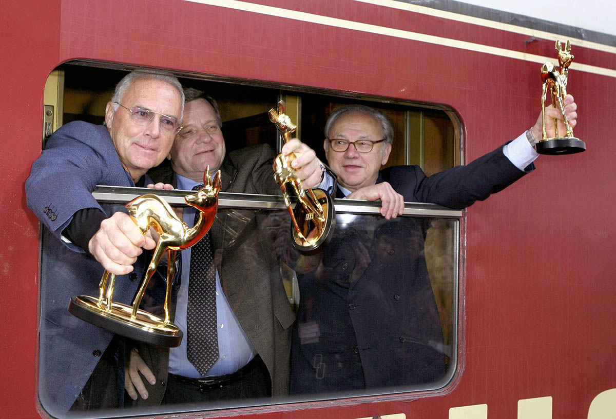 Франц Беккенбауэр, руководитель железной дороги Хартмут Медорн и издатель Хуберт Бурда представляют футбольные трофеи, 26 ноября 2005 года. Фото Reinhard Kurzendцrfer/IMAGO/Scanpix/LETA