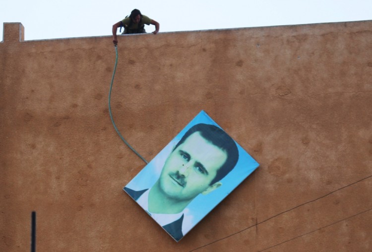 Член «Джабхат ан-Нусра» сбивает портрет Башара Асада с одного из изданий в провинции Идлиб. Фото: Reuters / Scanpix