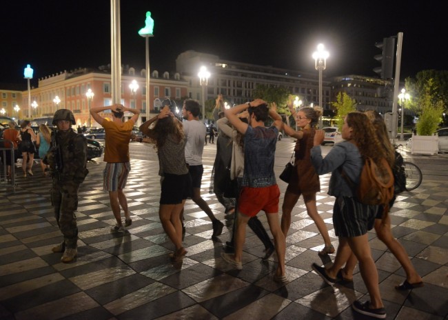 People cross the street with their hands on thier heads as a French soldier secures the area July 15, 2016 after at least 60 people were killed along the Promenade des Anglais in Nice, France, when a truck ran into a crowd celebrating the Bastille Day national holiday July 14.  REUTERS/Jean-Pierre Amet