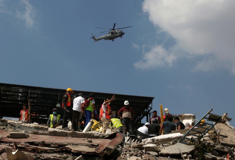A military helicopter flies over a collapsed building as rescue personnel look for people among the rubble after an earthquake hit Mexico City, Mexico September 19, 2017. REUTERS/Claudia Daut