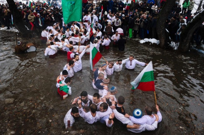 Men dance in the icy winter waters of the Tundzha river in the town of Kalofer as part of the Epiphany Day celebrations on January 6, 2016.  As a tradition, an Eastern Orthodox priest throws a cross in the river and it is believed that the one who retrieves it will be healthy through the year as well as all those who dance in the icy waters.  / AFP / DIMITAR DILKOFF
