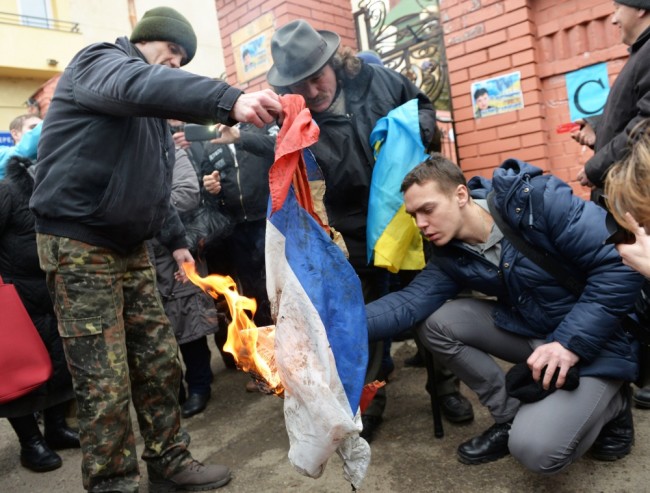 Activists burn the Russian flag at the Russian consulate in Lviv, western Ukraine, during the rally  in support of jailed Ukrainian pilot Nadiya Savchenko on March 9, 2016. A group of Ukrainians with scarves covering their faces threw smoke bombs and fireworks at the Russian mission in the western city of Lviv, while a local lawmaker tore down the Russian flag. The cultural capital of Ukraine was one of several cities staging protests against the trial in Russia of Nadiya Savchenko, a military pilot accused of being involved in the killing of two Russian reporters during the Ukraine conflict. / AFP / YURIY DYACHYSHYN