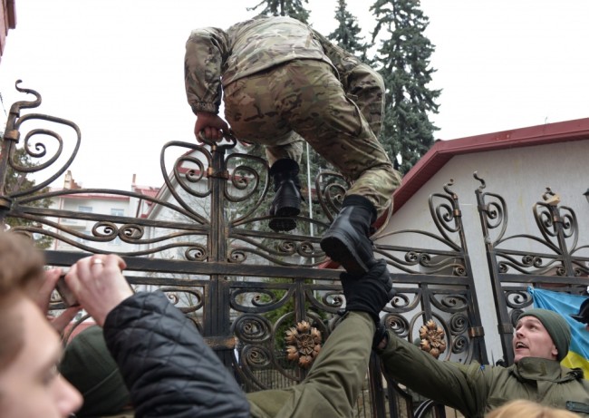 TOPSHOT - Activist climbs over the fence to the Russian consulate in Lviv, western Ukraine, during the rally in support of jailed Ukrainian pilot Nadiya Savchenko on March 9, 2016. A group of Ukrainians with scarves covering their faces threw smoke bombs and fireworks at the Russian mission in the western city of Lviv, while a local lawmaker tore down the Russian flag. The cultural capital of Ukraine was one of several cities staging protests against the trial in Russia of Nadiya Savchenko, a military pilot accused of being involved in the killing of two Russian reporters during the Ukraine conflict. / AFP / YURIY DYACHYSHYN