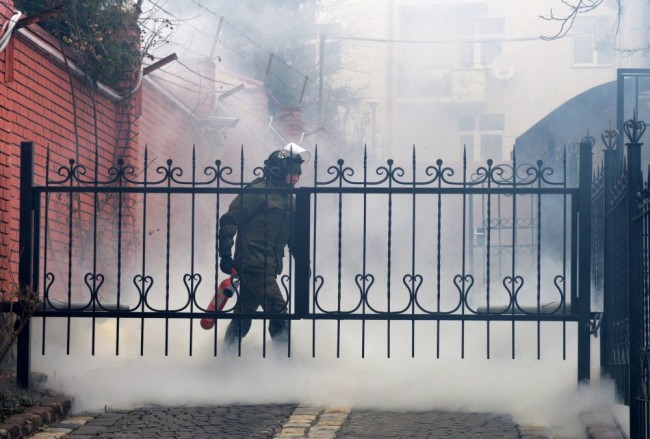 A member of security forces extinguishes a smoke bomb at the Russian consulate in Lviv, western Ukraine, during a rally in support of jailed Ukrainian military pilot Nadiya Savchenko on March 9, 2016. A group of Ukrainians with scarves covering their faces on March 9 threw smoke bombs and fireworks at the Russian mission in the western city of Lviv, while a local lawmaker tore down the Russian flag. The cultural capital of Ukraine was one of several cities staging protests against Savchenko's trial, accused of being involved in the killing of two Russian reporters during the Ukraine conflict. / AFP / YURIY DYACHYSHYN