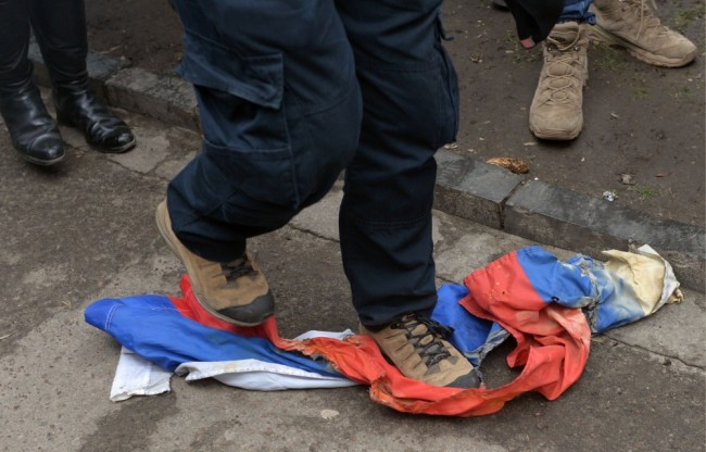 A protester tramples a Russian flag at Russian consulate in Lviv, western Ukraine, during a rally in support of jailed Ukrainian military pilot Nadiya Savchenko, on March 9, 2016. A group of Ukrainians with scarves covering their faces on March 9 threw smoke bombs and fireworks at the Russian mission in the western city of Lviv, while a local lawmaker tore down the Russian flag. The cultural capital of Ukraine was one of several cities staging protests against Savchenko's trial, accused of being involved in the killing of two Russian reporters during the Ukraine conflict. / AFP / YURIY DYACHYSHYN
