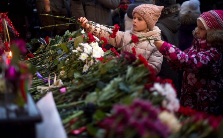 Two girls lay flowers at the home stage building of the Alexandrov Ensemble (The Red Army Choir), in Moscow, on December 25, 2016, after a Russian military plane which included dozens of Red Army Choir members crashed.  The Russian military plane crashed on its way to Syria on December 25, with no sign of survivors among the 92 onboard, who included dozens of Red Army Choir members heading to celebrate the New Year with troops. Russia's defence ministry said a body had been recovered from the Black Sea. / AFP PHOTO / Alexander UTKIN