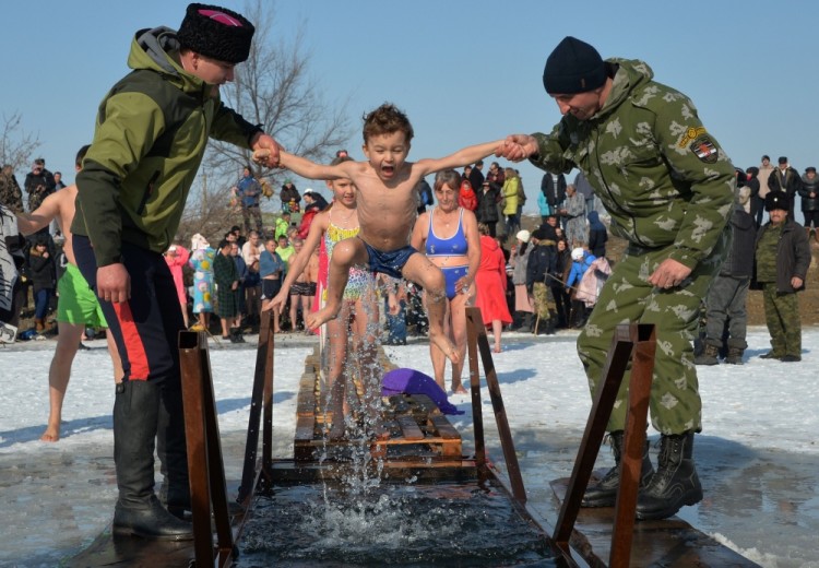 Cossacks help a boy to take a bath in the icy waters of a lake during the celebration of the Epiphany holiday near the village of Leninskoe, some 15 km of Bishkek, on January 19, 2017. / AFP PHOTO / Vyacheslav OSELEDKO