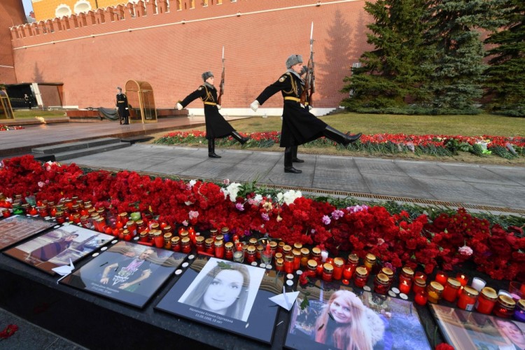 Flowers and candles left in tribute to the victims of the April 3 blast in the Saint Petersburg metro are seen by a memorial stone reading Leningrad by the Kremlin wall as honour guard soldiers march during the changing of the guards ceremony in central Moscow on April 6, 2017. / AFP PHOTO / Natalia KOLESNIKOVA