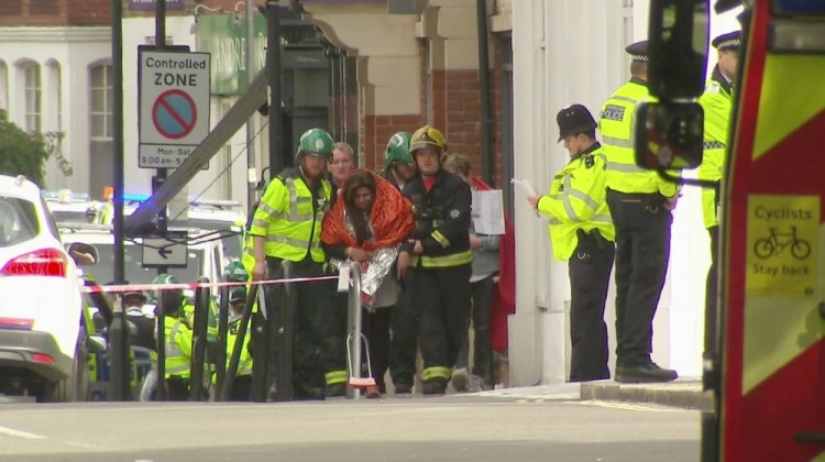 In this image made from video, a woman with blankets wrapped around her is being escorted  by emergency services near the scene of an explosion in London Friday, Sept. 15, 2017. A reported explosion at a train station sent commuters stampeding in panic, injuring several people at the height of London's morning rush hour, and police said they were investigating it as a terrorist attack. (Sky via AP)