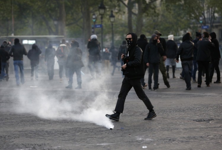 Youths walk near tear gas grenades as the scuffle with riot police officers during a protest in Paris , Sunday April 23, 2017. Protesters angry that far-right leader Marine Le Pen is advancing the French presidential runoff are scuffling with police in Paris. (AP Photo/Kamil Zihnioglu)
