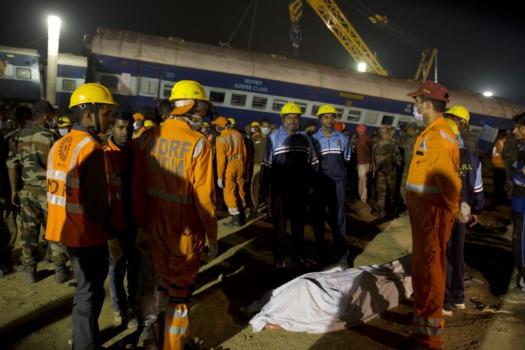 Rescuers stand near the body of a victim to wait for ambulance after 14 coaches of an overnight passenger train rolled off the track near Pukhrayan village, Kanpur Dehat district, Uttar Pradesh state, India, Sunday, Nov. 20, 2016. Scores of people were killed in the accident. (AP Photo/Rajesh Kumar Singh)