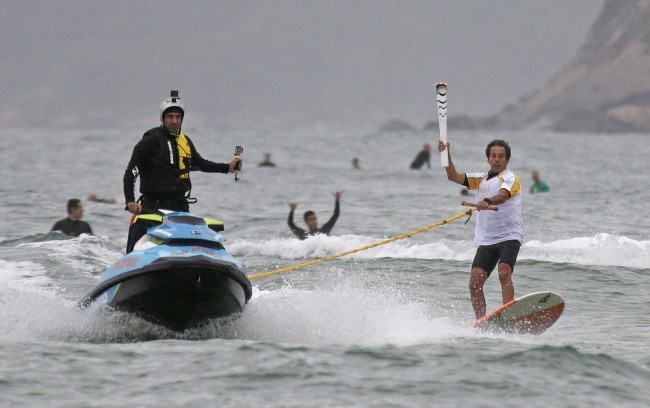 Бразильский серфер продолжает эстафету олимпийского огня. Фото: AP Photo / Scanpix