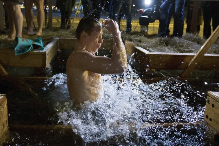 A Russian Orthodox believer crosses himself as he bathes in the icy water on Epiphany at the Church of the Holy Trinity, left, in Ostankino near TV Tower in Moscow, Russia, Wednesday, Jan. 18, 2017. Water that is blessed by a cleric on Epiphany is considered holy and pure until next year's celebration, and is believed to have special powers of protection and healing. The Russian Orthodox Church follows the old Julian calendar, according to which Epiphany falls on Jan. 19. (AP Photo/Alexander Zemlianichenko Jr)