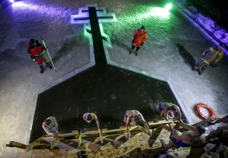 Russian Orthodox believers dip in the icy water in a hole in the form of Orthodox Cross on Epiphany at a pond in Tyarlevo village outside St.Petersburg, Russia, early Thursday, Jan. 19, 2017. The temperature in St. Petersburg is minus 2 degrees Centigrade (28 degrees Fahrenheit). Thousands of Russian Orthodox Church followers plunged into icy rivers and ponds across the country to mark Epiphany, cleansing themselves with water deemed holy for the day. Water that is blessed by a cleric on Epiphany is considered holy and pure until next year's celebration, and is believed to have special powers of protection and healing. (AP Photo/Dmitri Lovetsky)