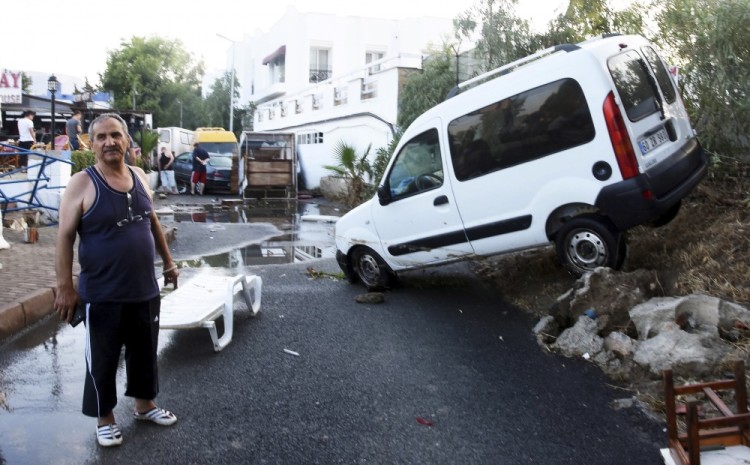 A man walks past a car, damaged in the overnight earthquake is seen in Bodrum, Turkey, Friday, July 21, 2017. A powerful earthquake sent a building crashing down on tourists at a bar on the Greek holiday island of Kos and struck panic on the nearby shores of Turkey early Friday, killing two people and injuring some 200 people. (DHA-Depo Photos via AP)